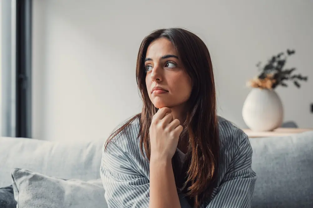 A woman looks upward thoughtfully beside a window.