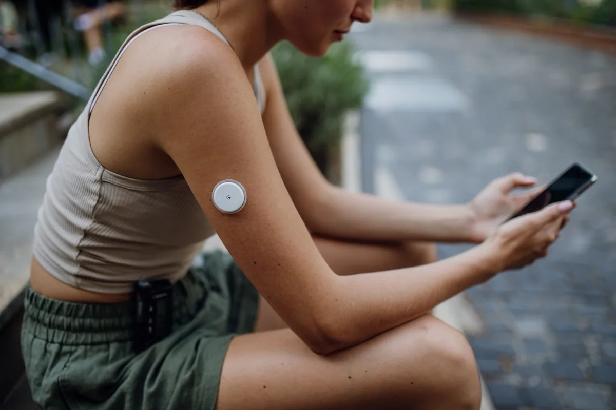 A person checks a small medical sensor on their upper arm using a phone.