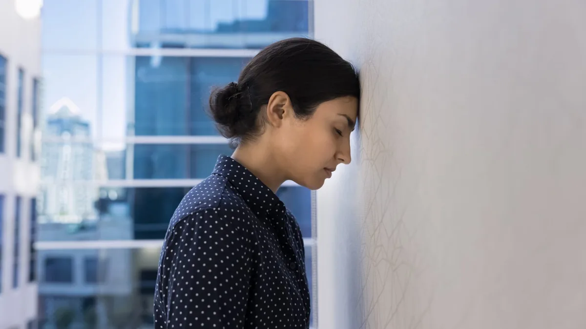 A woman takes a thoughtful pause beside a window.