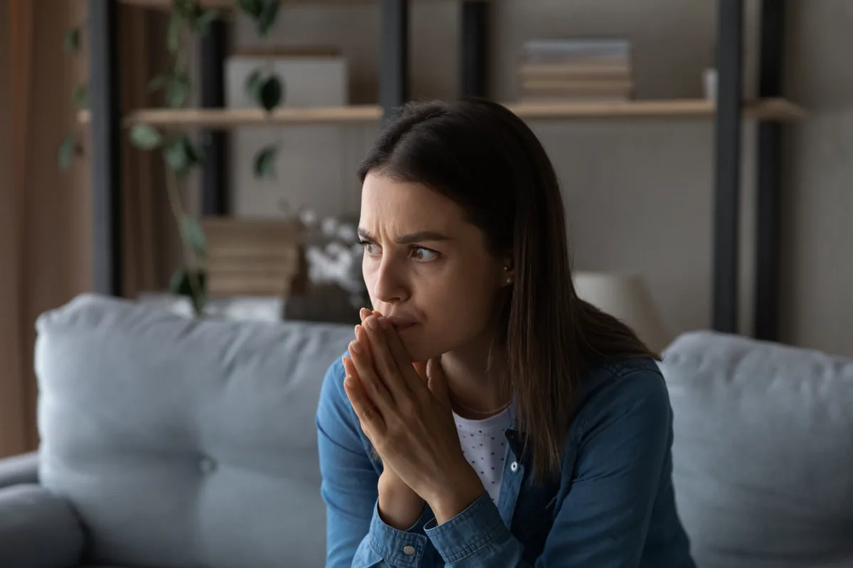 A woman pauses thoughtfully while sitting on a sofa.