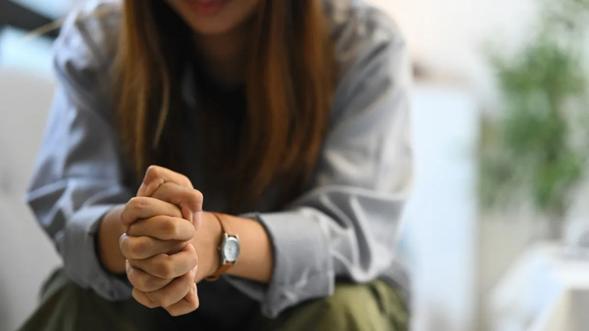 A person sits with their hands resting together in their lap.