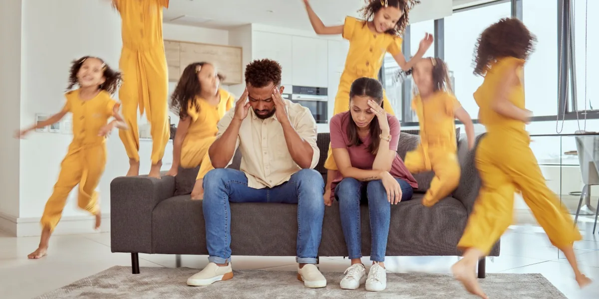 A family sits together on a sofa while children move around the room.