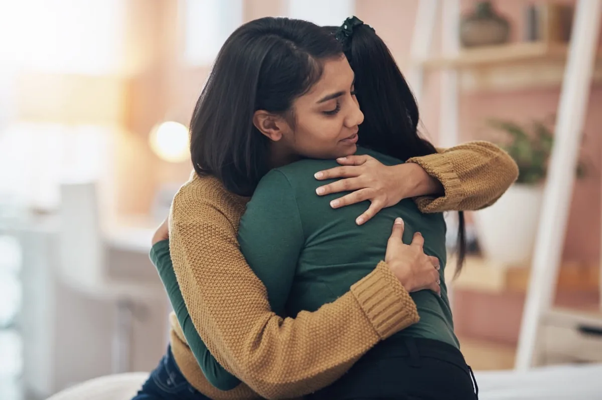 Two people share a comforting hug indoors.