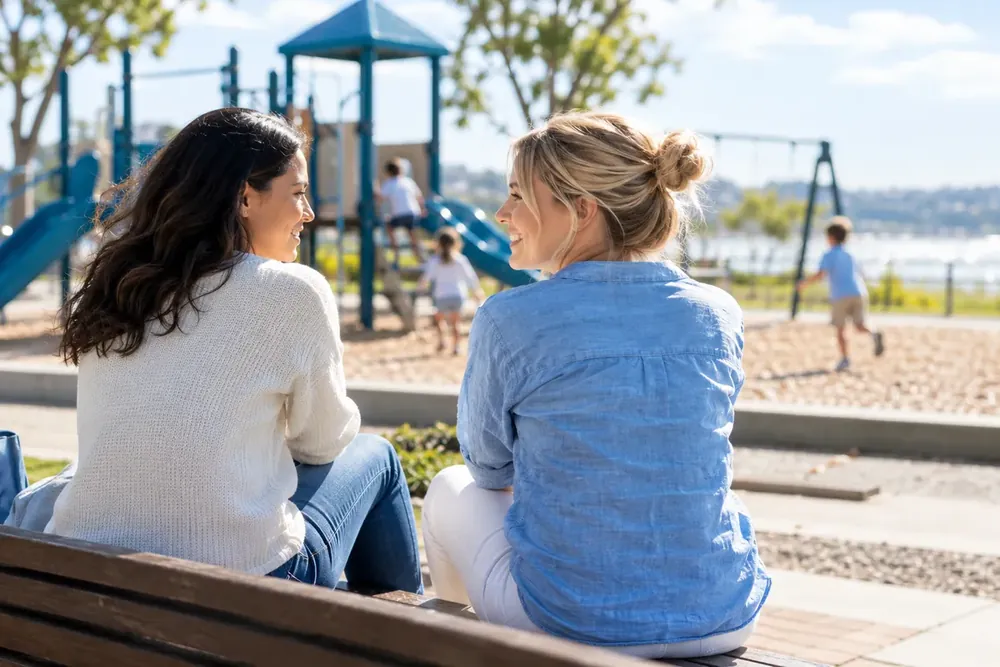 Two adults talking beside a sunny playground