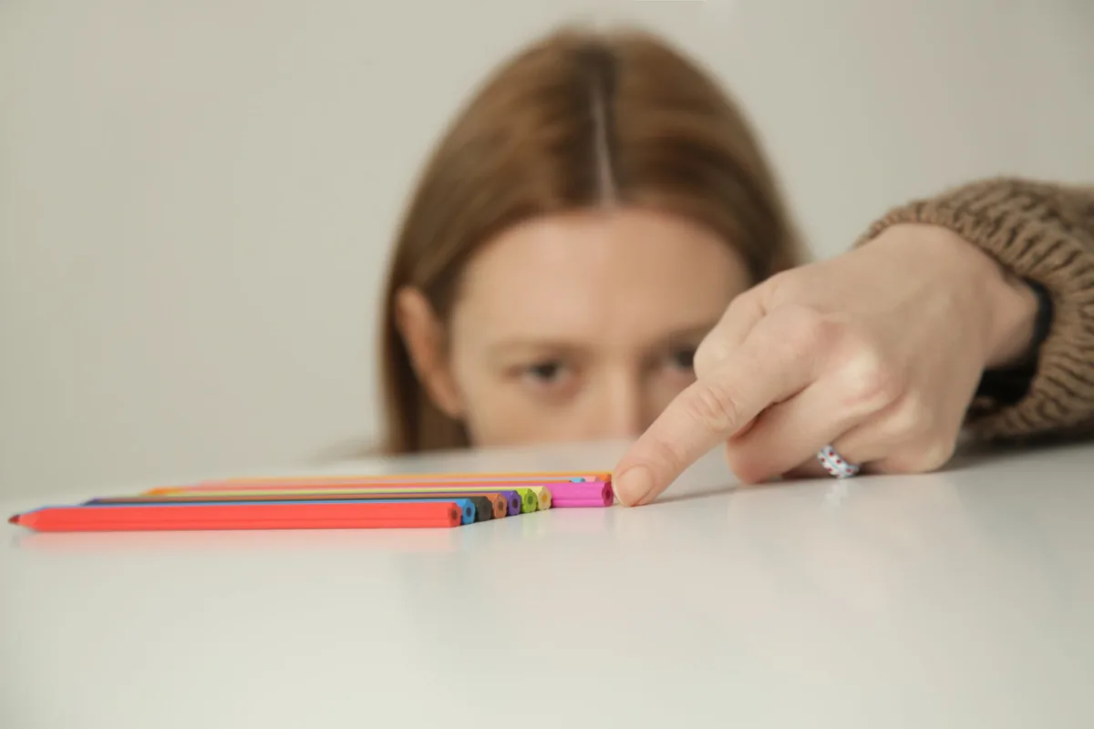 A child watches closely as an adult points to colored pencils.