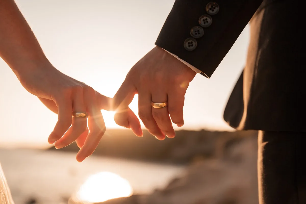 Two people gently link fingers in the warm evening light.