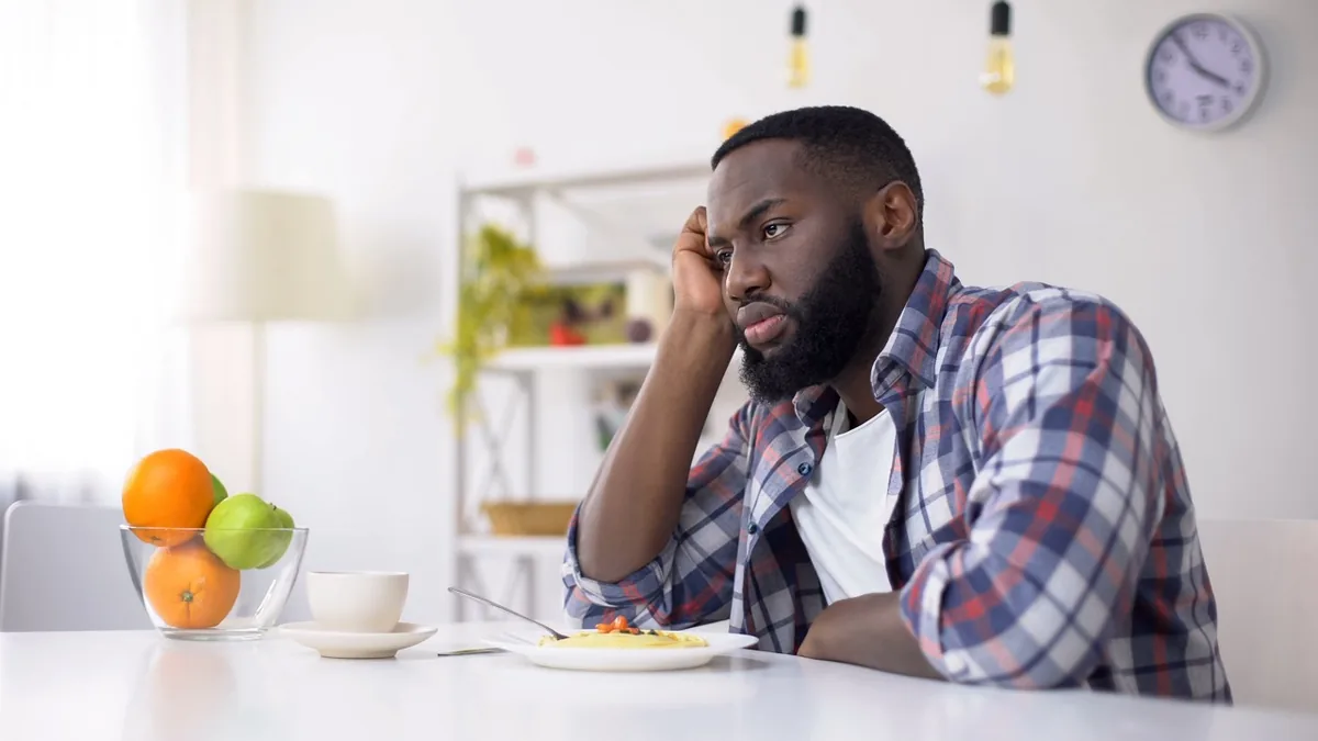 A man sits thoughtfully at a kitchen table.
