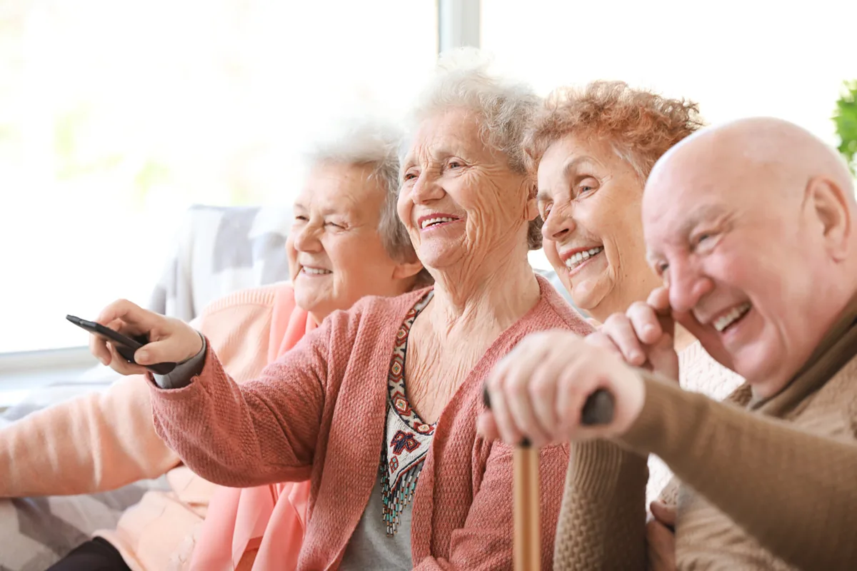 Older friends smile and gesture while sitting together on a sofa.