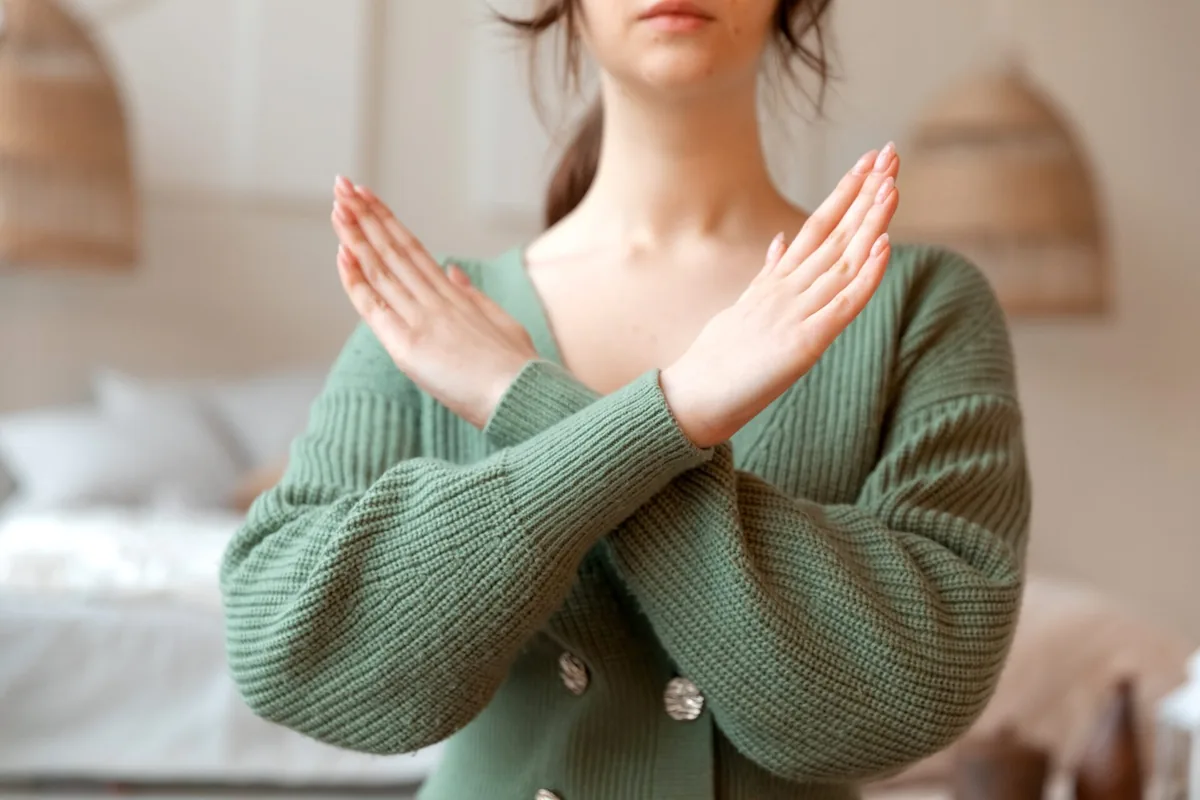 A woman raises her crossed hands in front of her as a boundary gesture.