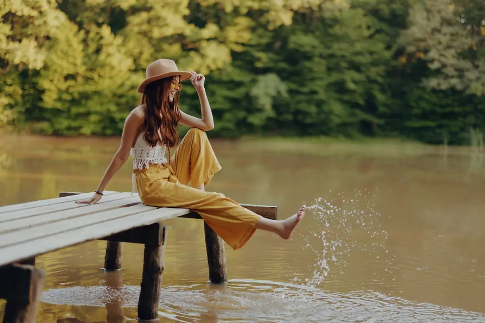 A woman relaxes beside a lake beneath green trees.