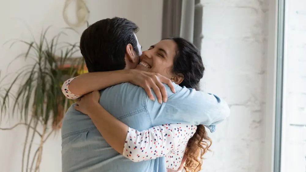 Two people embrace in a bright room.