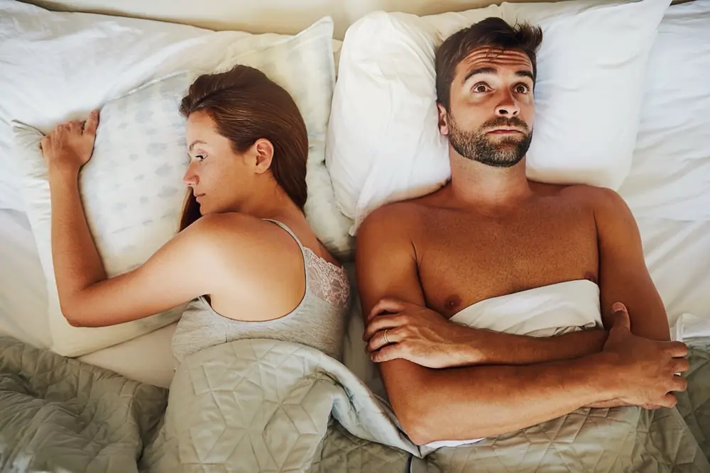 Two adults lie apart in a bed.