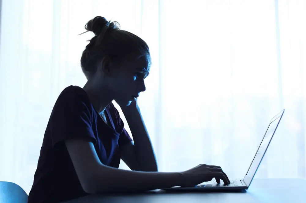 A seated person looks toward a bright laptop screen.
